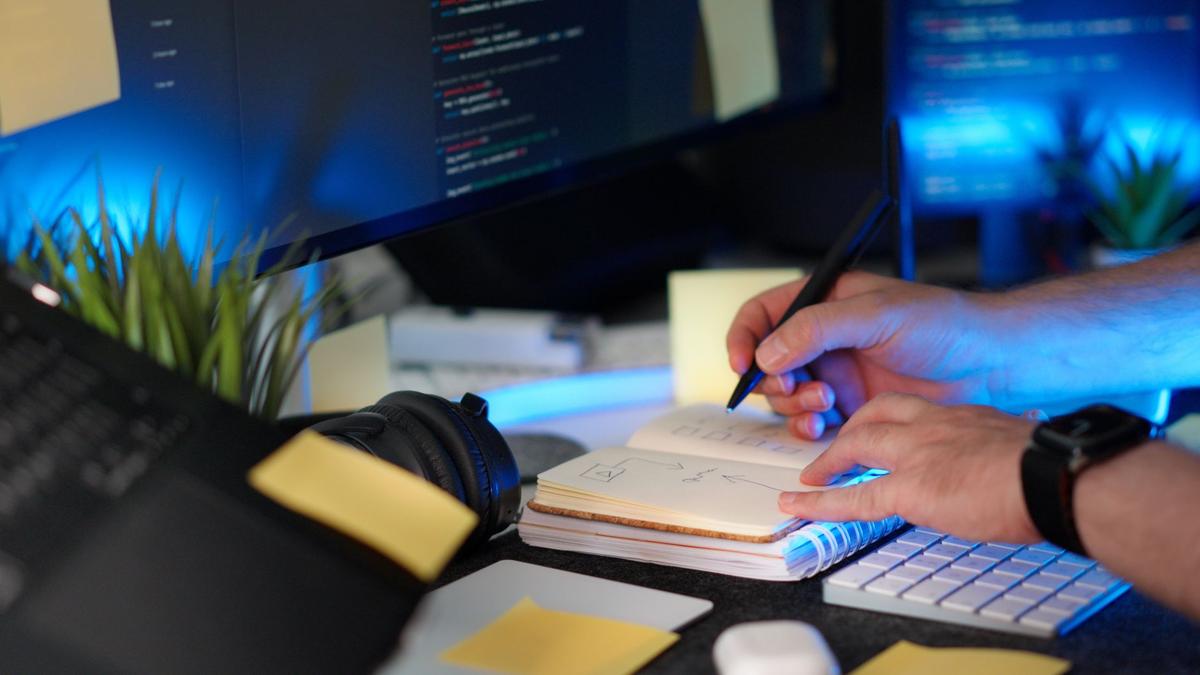 Handwritten planning notes beside a monitor showing code in a modern software workspace