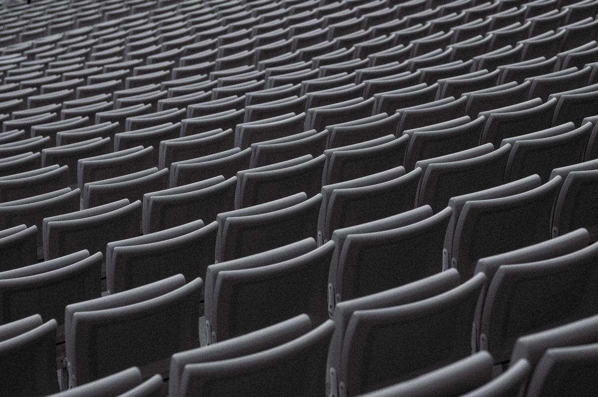 Endless rows of empty grey chairs receding into the distance in a large empty auditorium