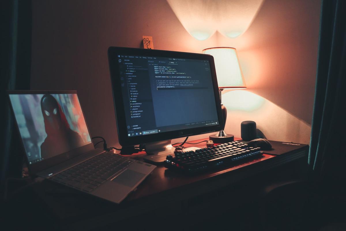 Warmly lit home office desk with dual monitors displaying code, a modern programming workspace