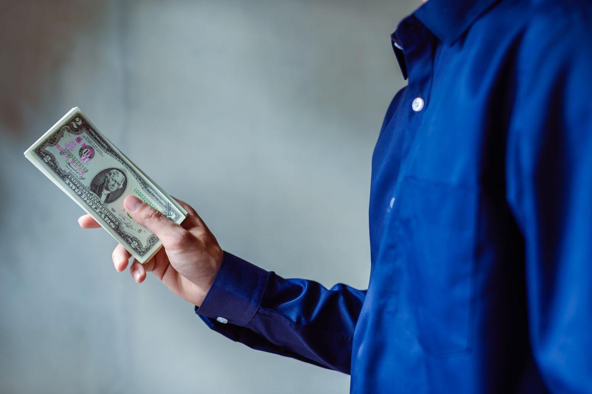 Person in a blue shirt holding a fanned stack of US dollar bills