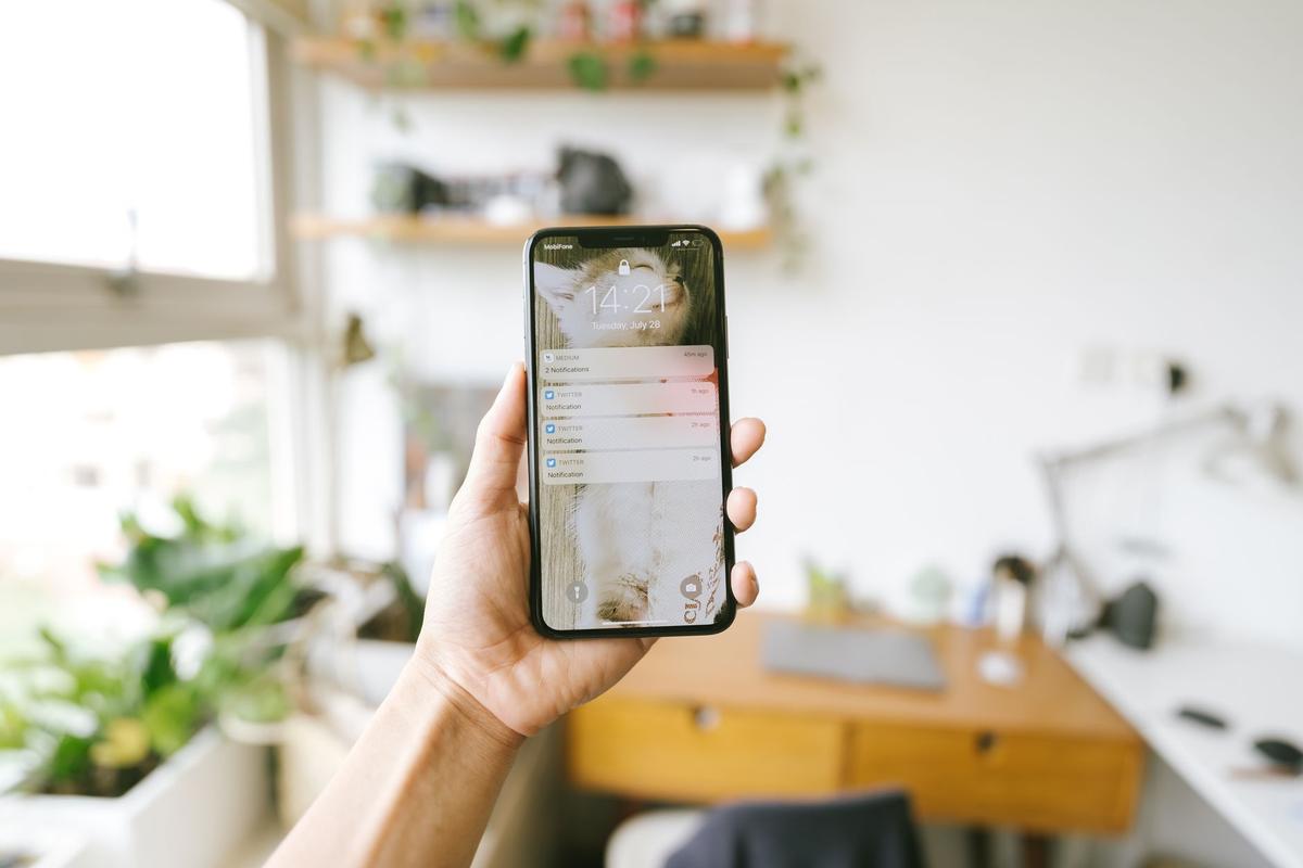 Hand holding a smartphone indoors with a blurred office background, focus on the screen notifications