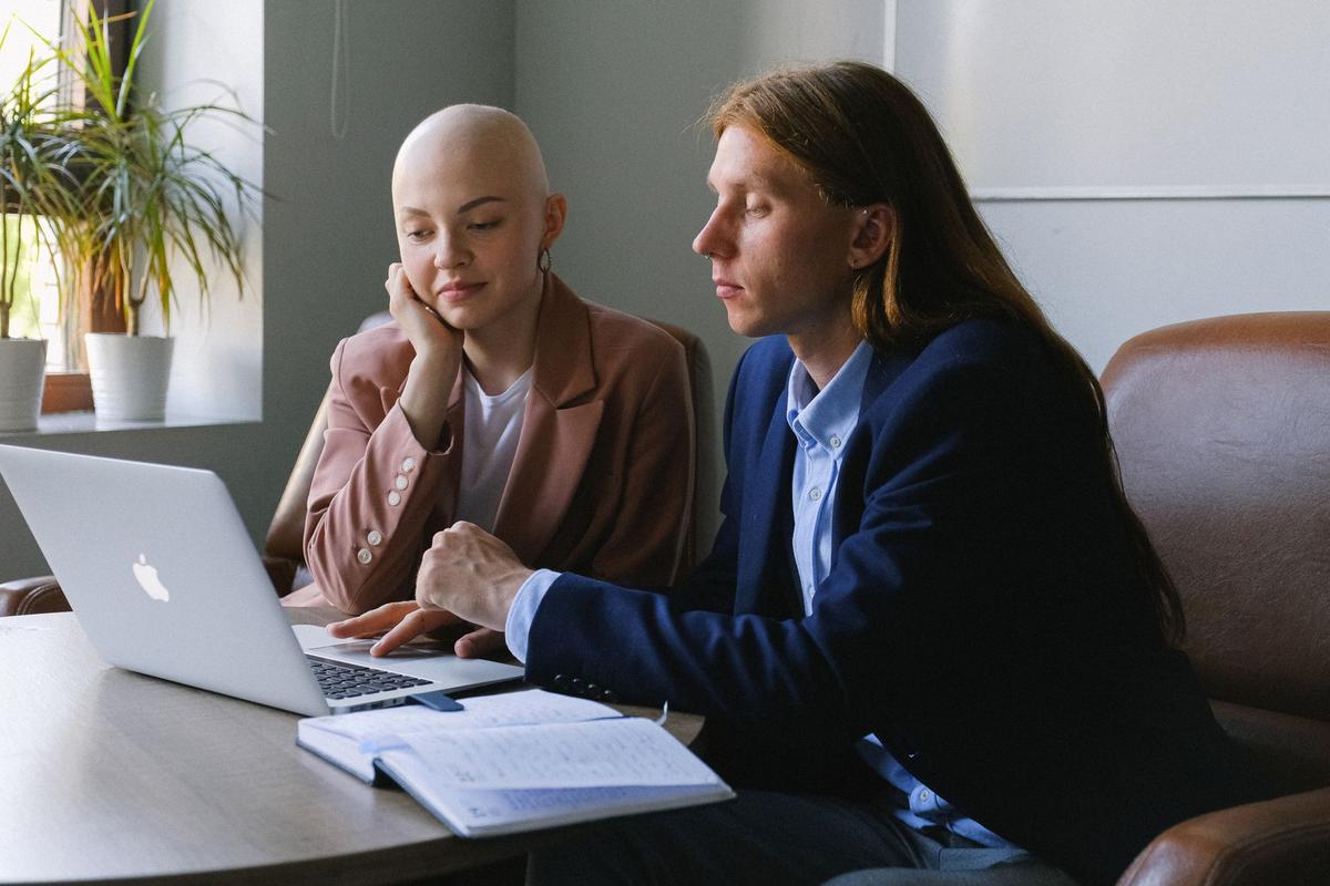 Man and woman in formal clothes sitting together at a table with a laptop and planner, working