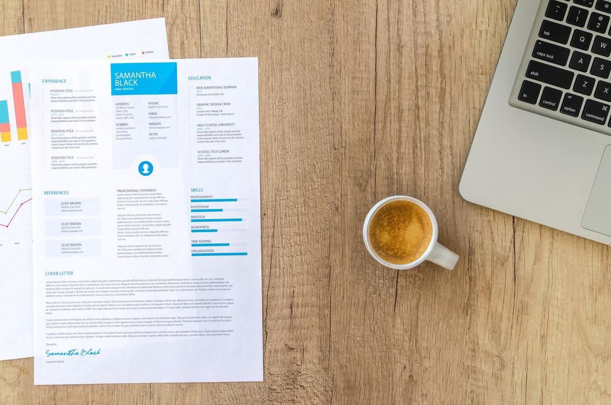 Top view of a resume, coffee cup, and laptop on a wooden desk