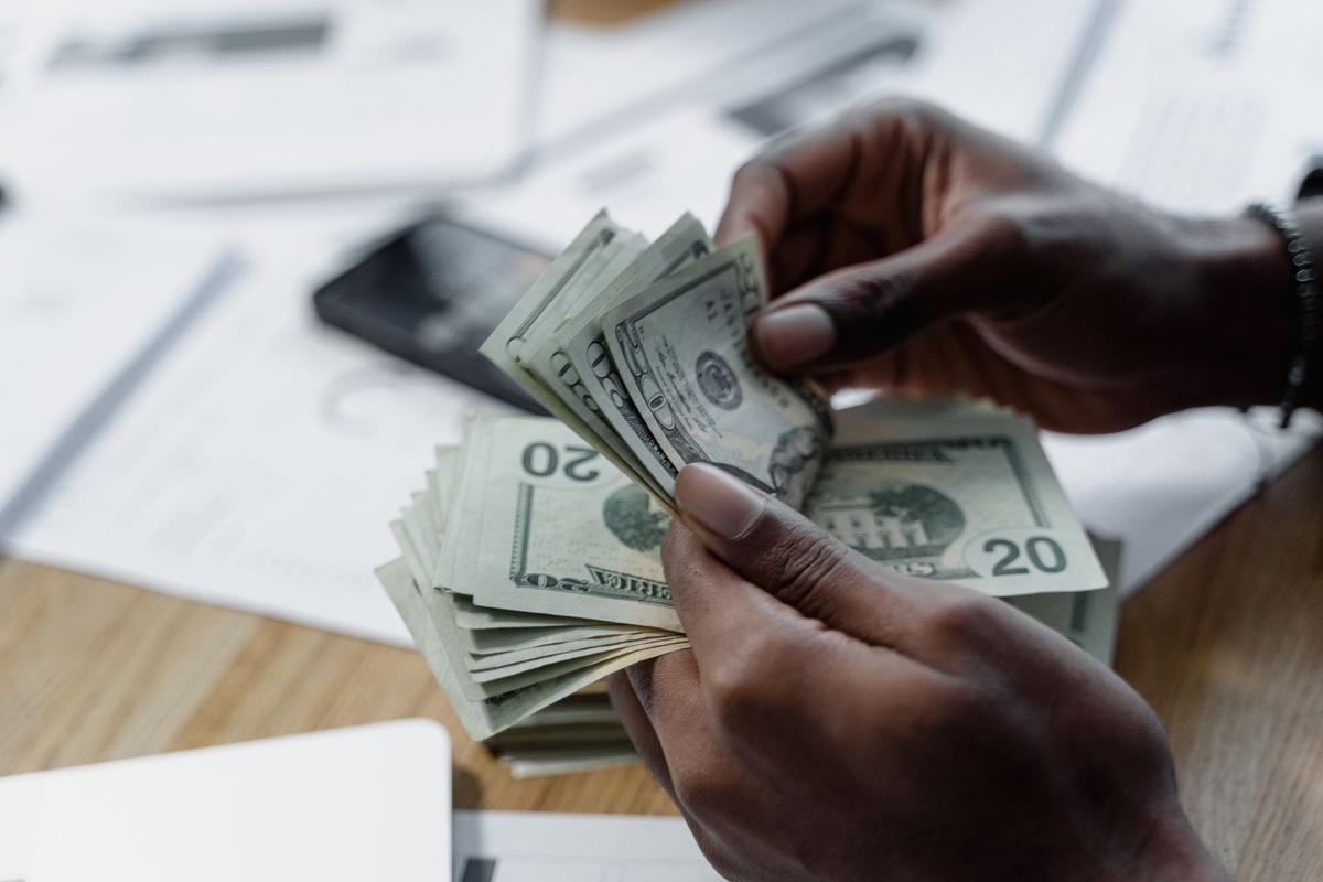 Close-up of hands counting US dollar bills on a wooden table with documents and a smartphone nearby