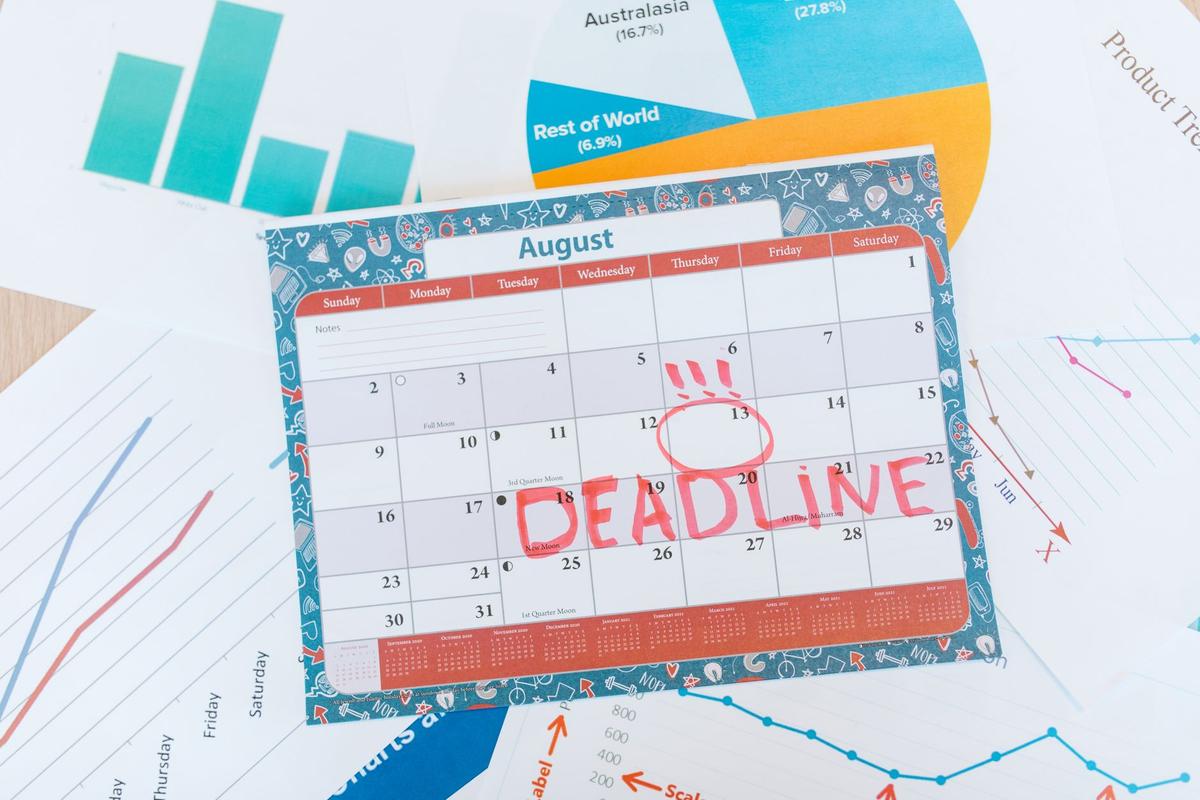 August calendar on a desk with a deadline marked in red, surrounded by graphs and charts.