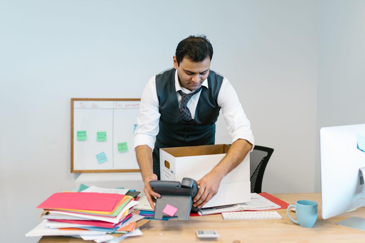 A man packing up his desk in an office with scattered papers and a phone