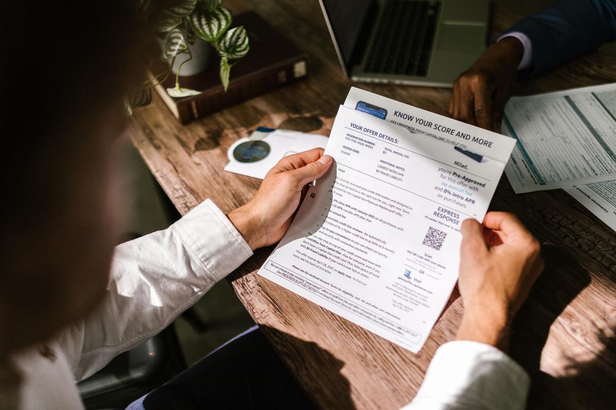 A man examining a financial document under natural light at a wooden desk