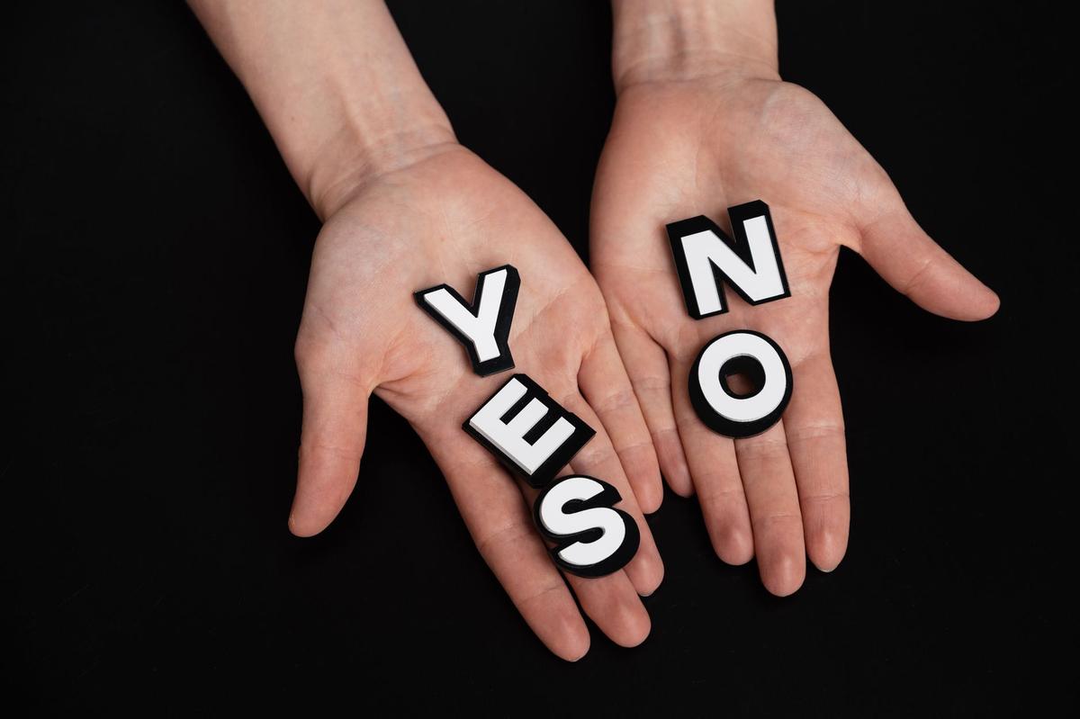 Two hands holding black and white letters spelling 'YES' and 'NO' on a black background