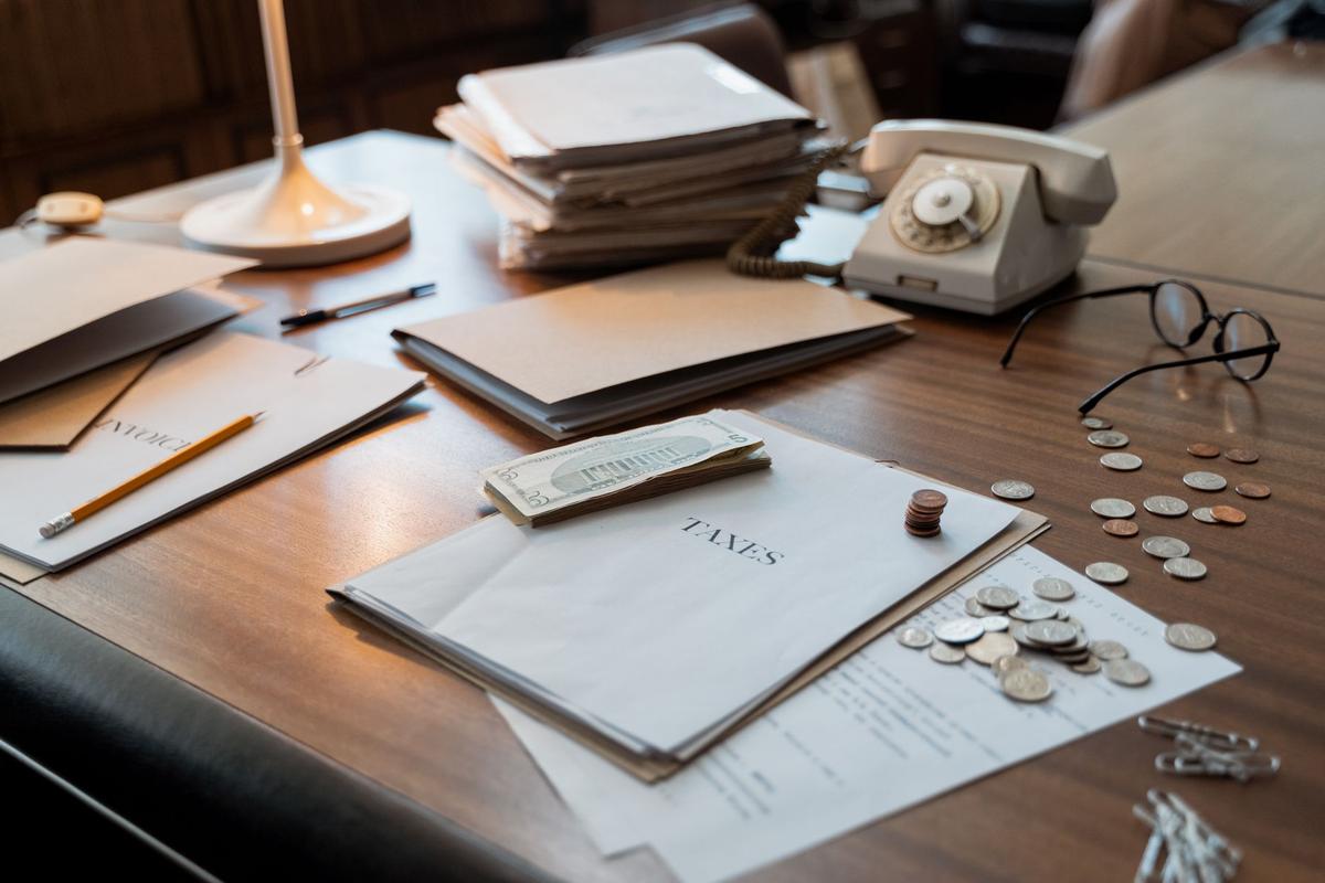 Office desk close-up with tax documents, coins, eyeglasses, and an old phone