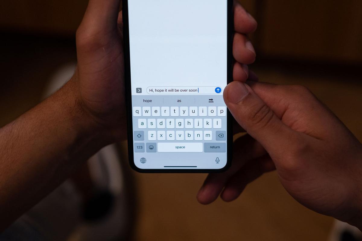 Close-up of hands texting on a smartphone indoors with a message visible on screen